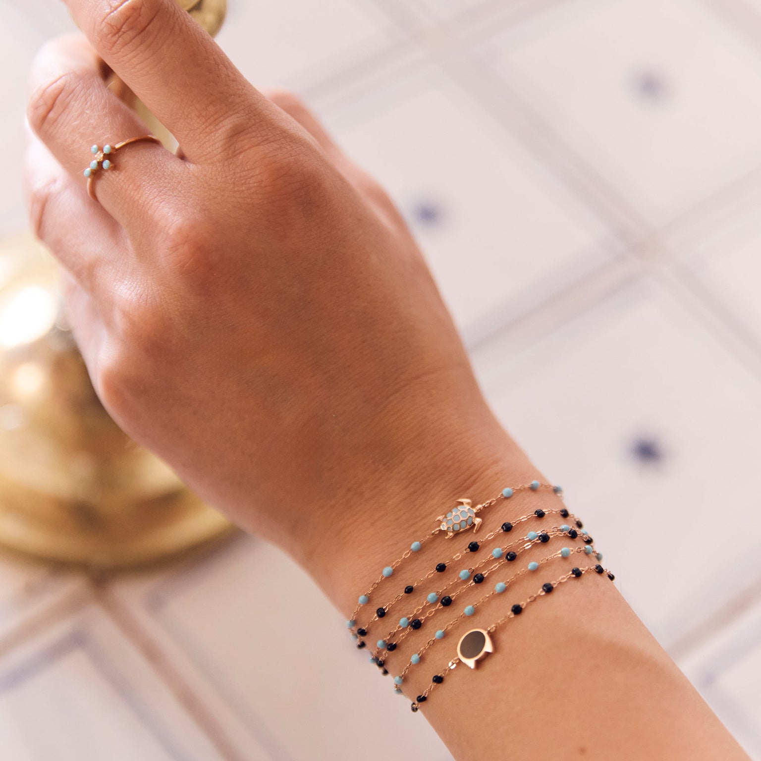 Photo de la main d’une femme portant différents bracelets Gigi Clozeau aux couleurs turquoise et noires.