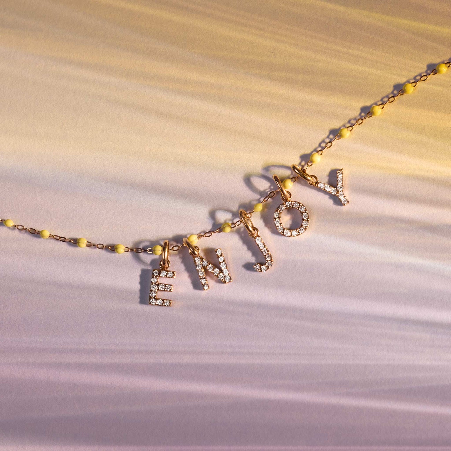 Photo de bijoux posés sur un fond, avec un collier et des pendentifs Lucky Letters diamantés Gigi Clozeau.